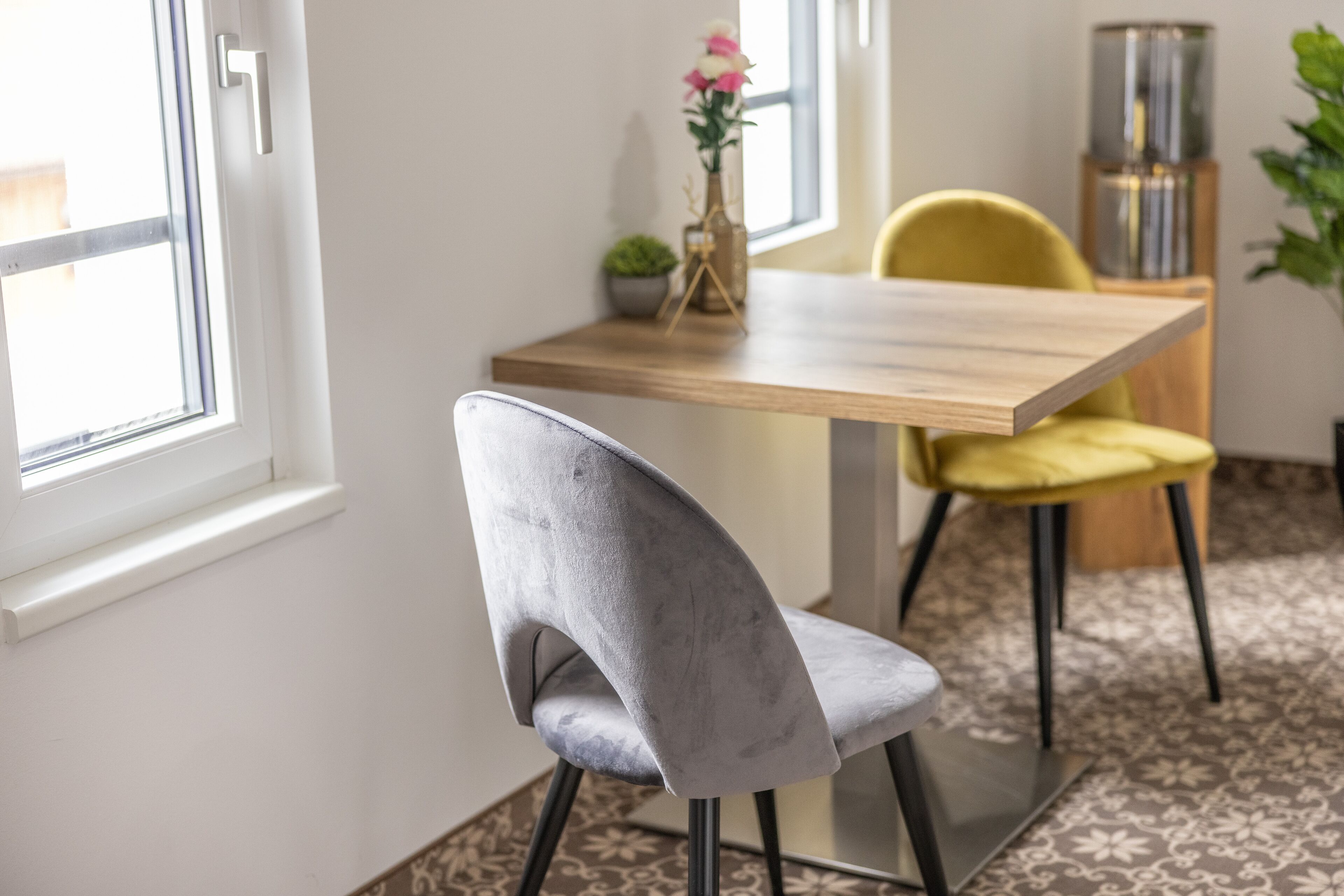 Un comedor con una mesa de madera y dos sillas, una gris y otra amarilla, con una planta en maceta sobre la mesa.