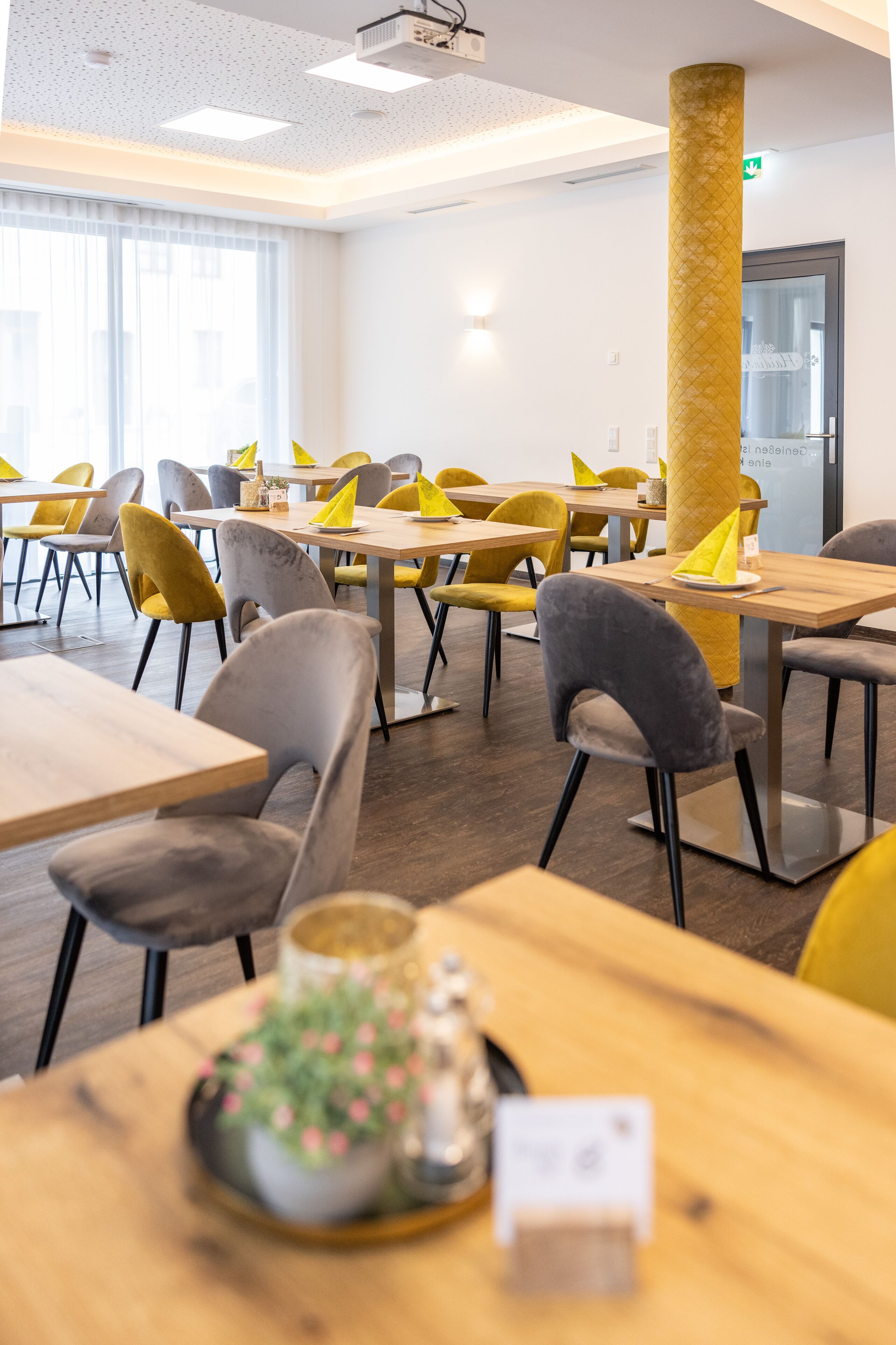 A modern dining area with wooden tables and chairs, a large pillar, and a potted plant on a table.