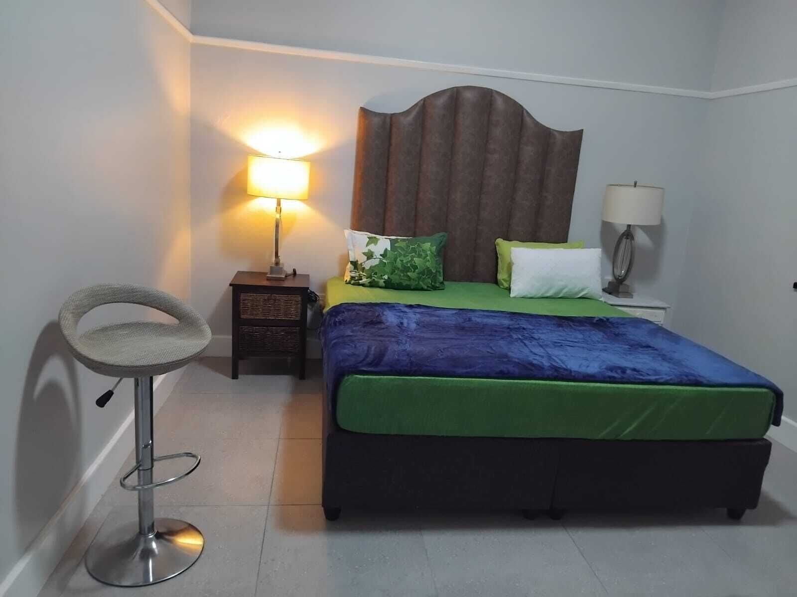 A bedroom with a bed, two bedside tables, a lamp, a chair, and a wall-mounted shelf.