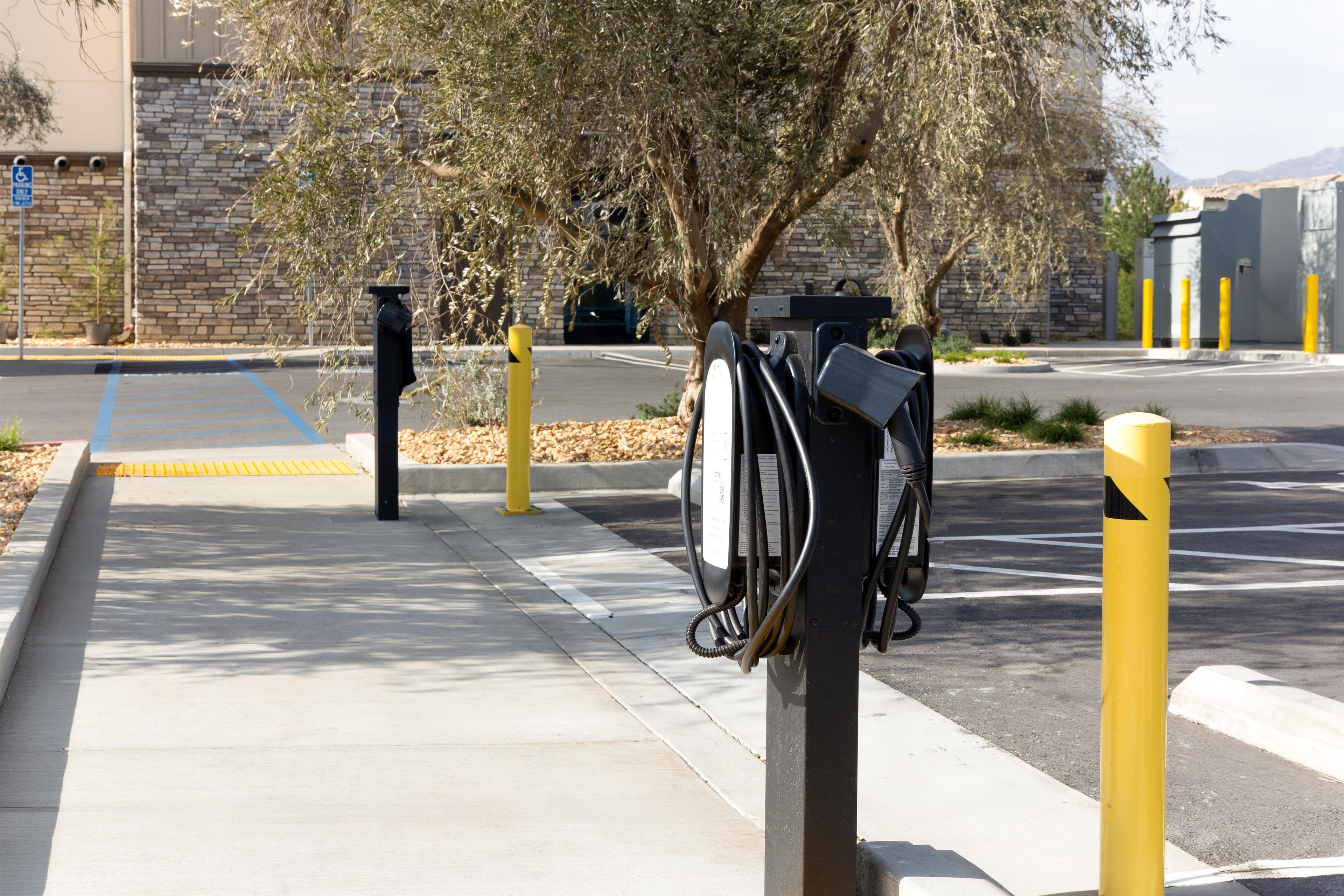 A parking area with electric vehicle charging stations, a clear pedestrian path, and a stone building in the background.