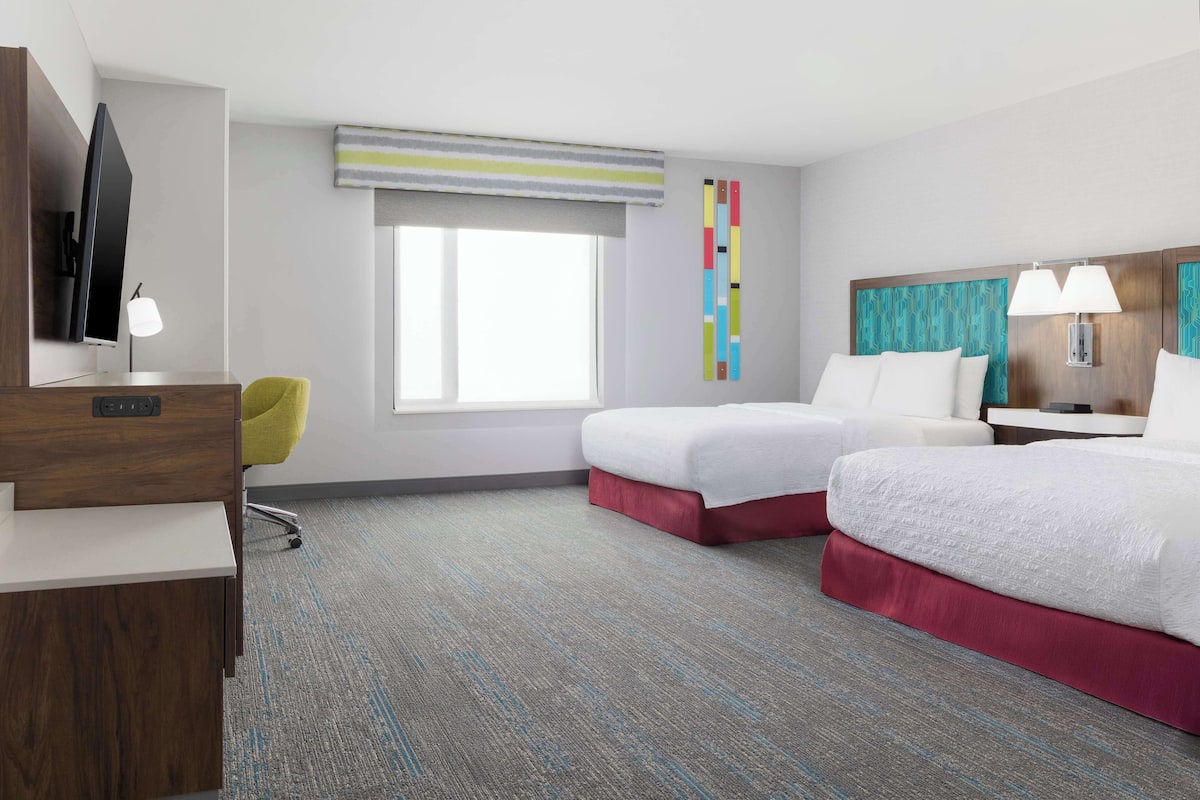 A hotel room with two beds, a desk, a chair, a TV, and a window with a view.