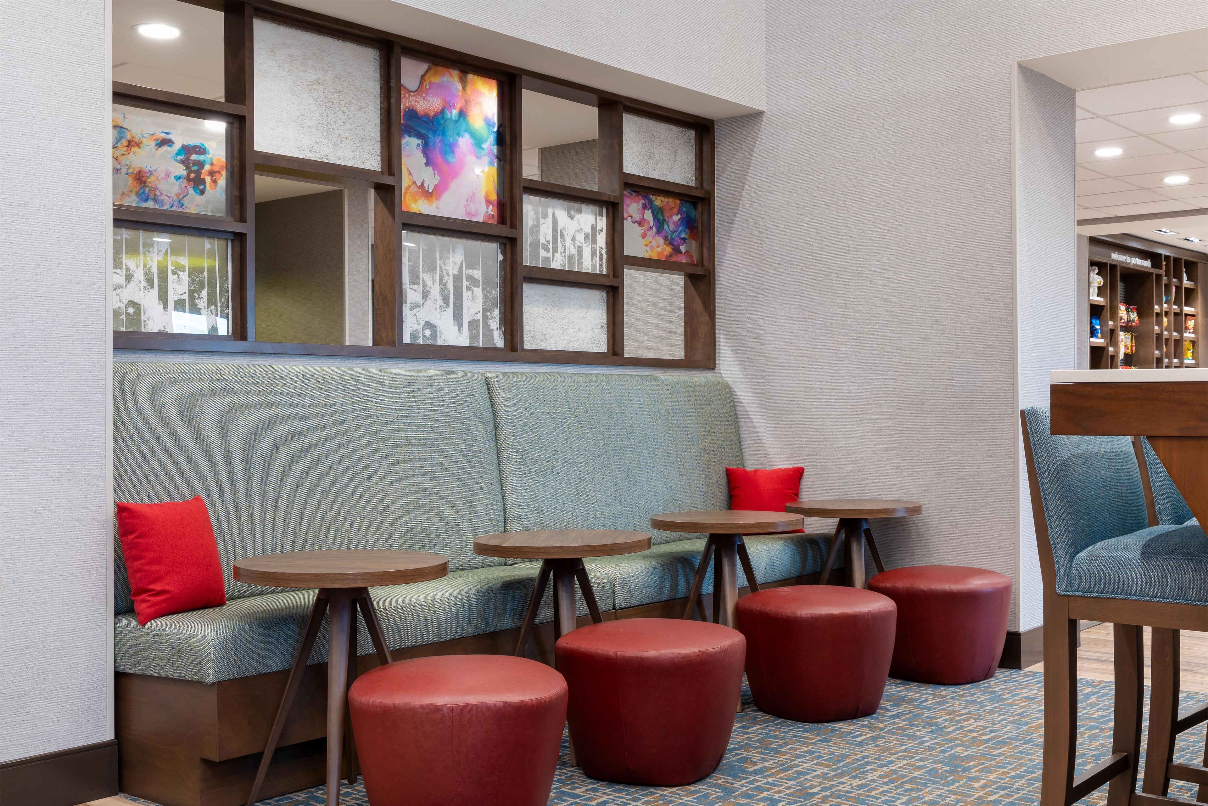 A seating area with a sofa, red ottomans, and small round tables.