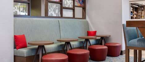 A seating area with a sofa, red ottomans, and small round tables.