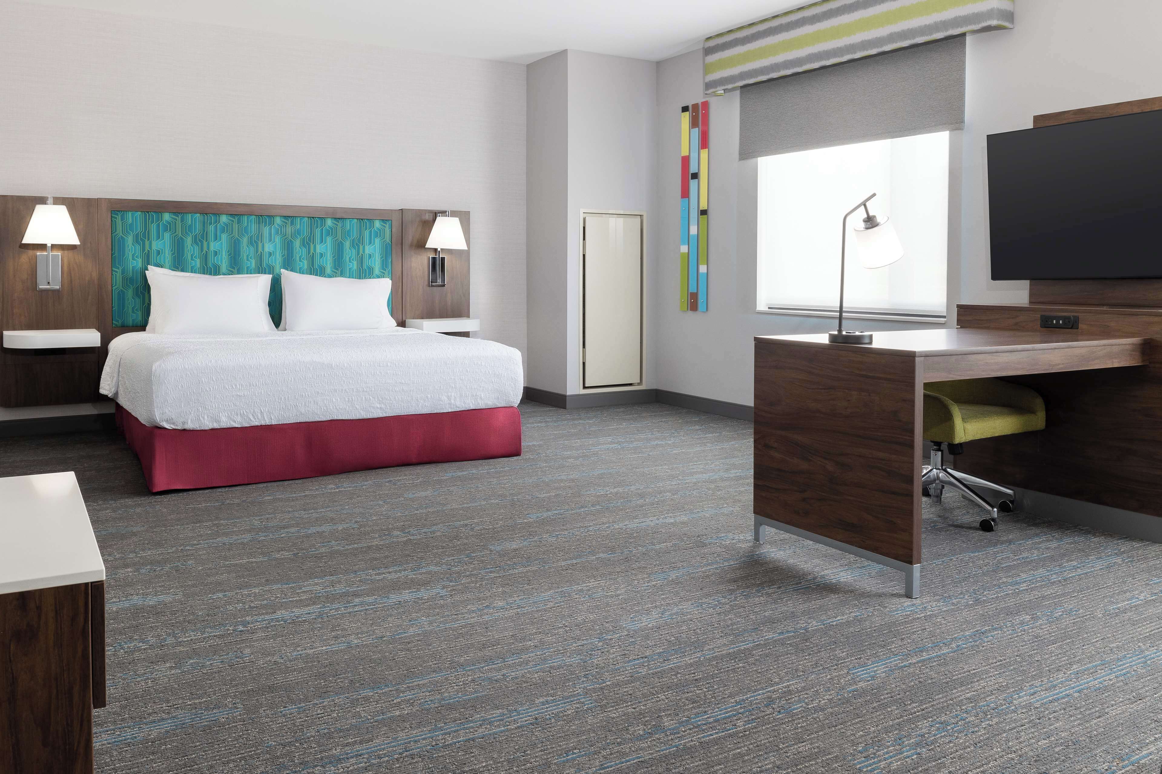 A modern hotel room with a bed, desk, and TV.