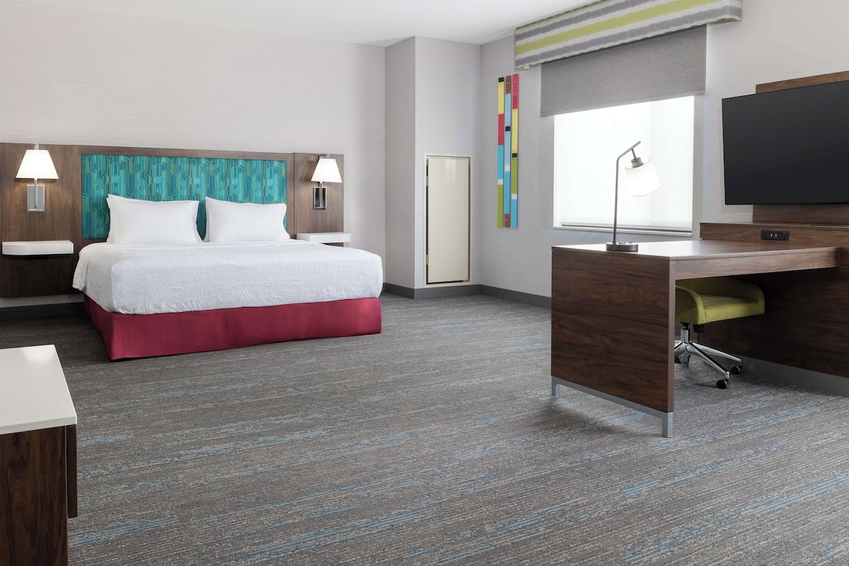 A modern hotel room with a bed, desk, and TV.