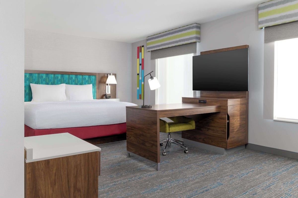 A hotel room with a bed, desk, and TV.