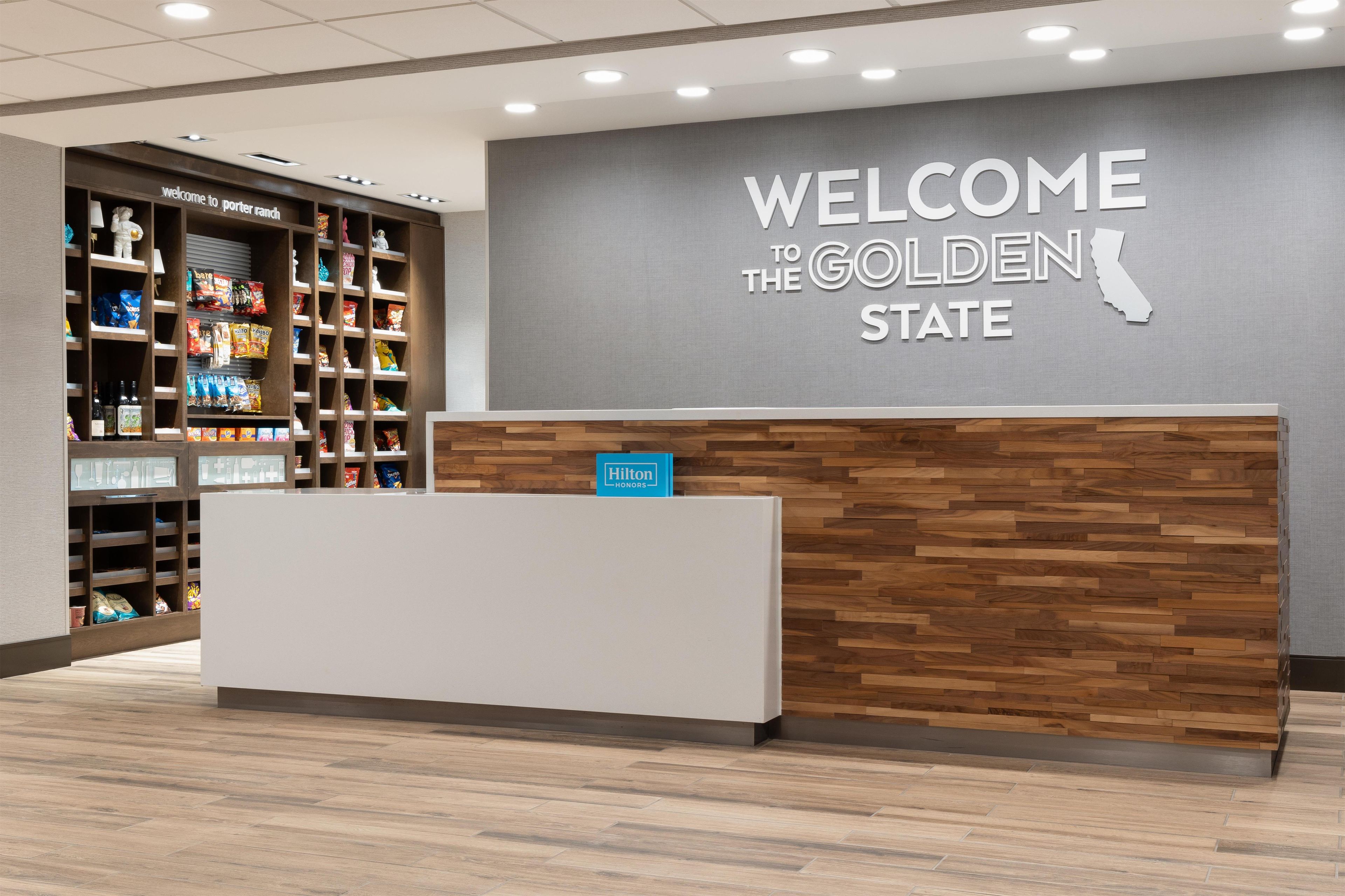 Een receptiebalie met een bordje 'Welcome to the Golden State', een minibar en een etalage met snacks.