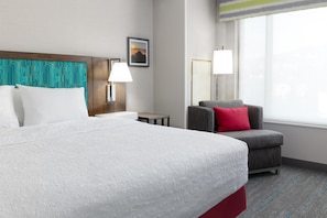 A hotel room with a large bed, a grey armchair with a red pillow, a nightstand with a lamp, and a picture on the wall. - Hampton Inn & Suites Porter Ranch Los Angeles (Porter Ranch)