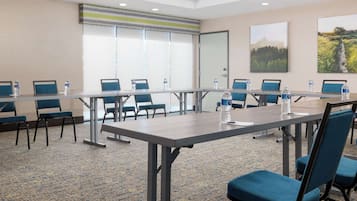 Un salón de conferencias con una mesa larga, sillas azules y botellas de agua.