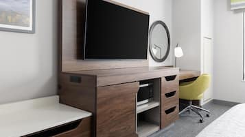 A hotel room with a bed, a desk, a television, a mirror, and a chair.