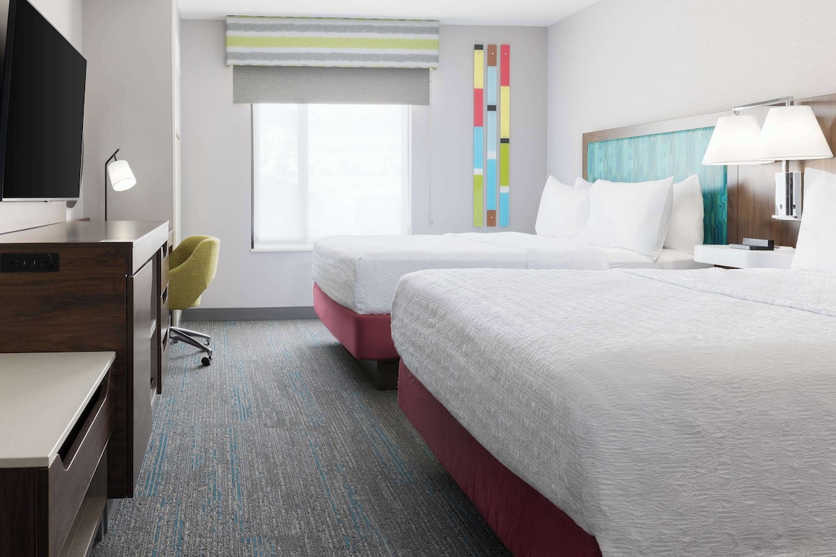 A hotel room with two beds, a desk, a chair, a TV, and a window with a view.