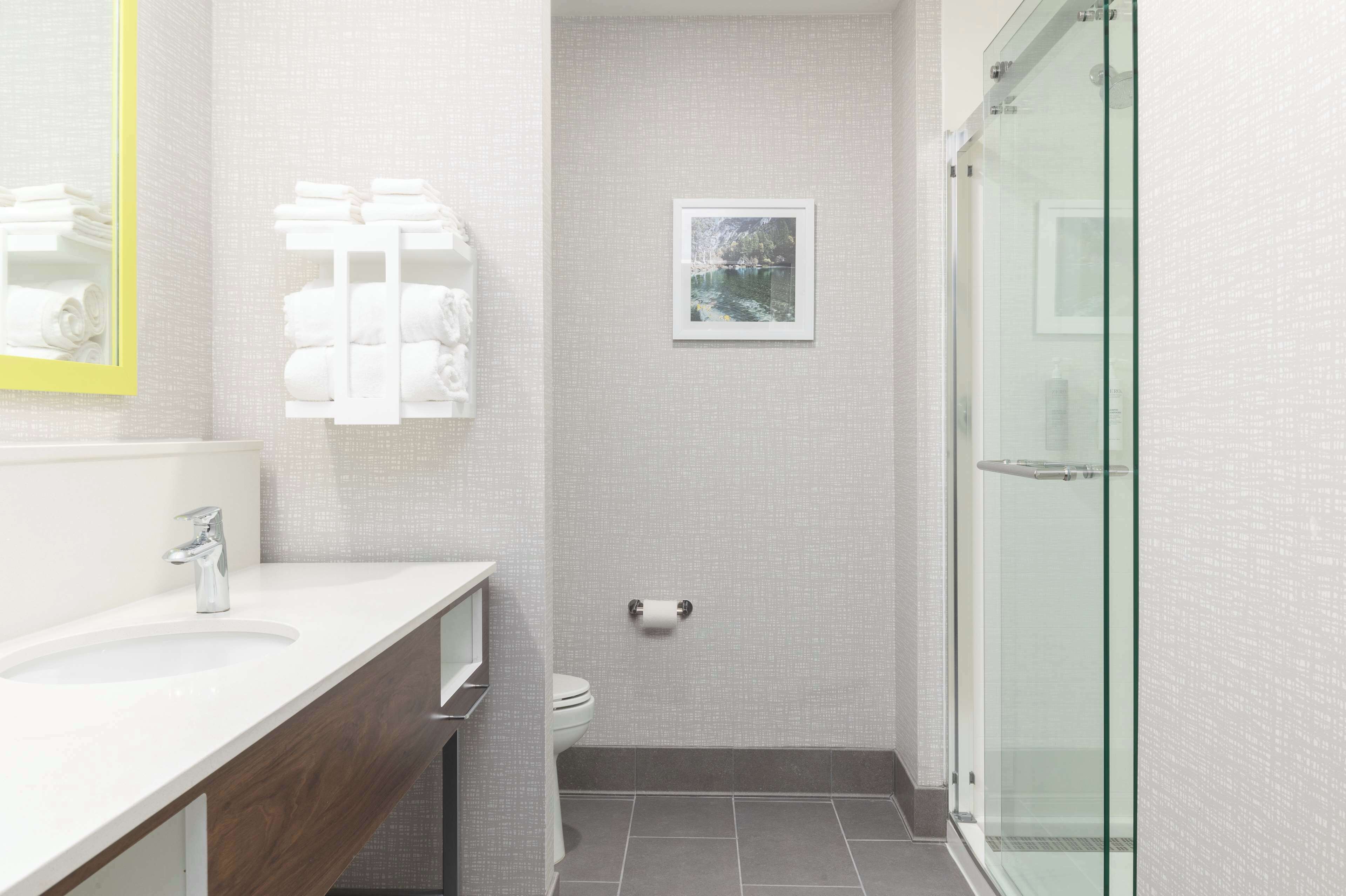 Un baño moderno con lavamanos blanco, espejo, inodoro y cabina de ducha con mampara de cristal.