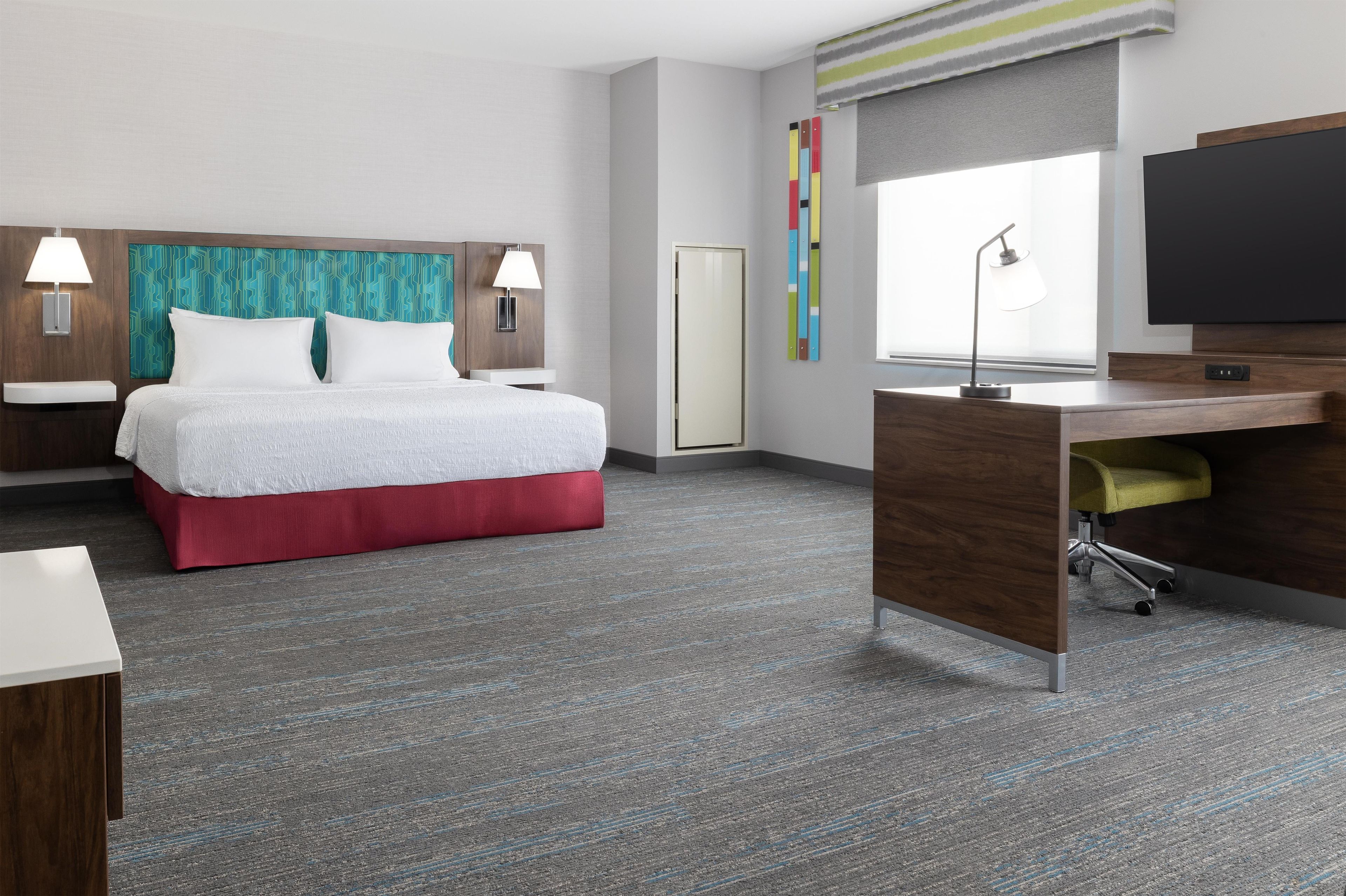 A hotel room with a bed, desk, and television.