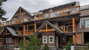 En fleretages hytte med træfacade, balkoner og en stensokkel.