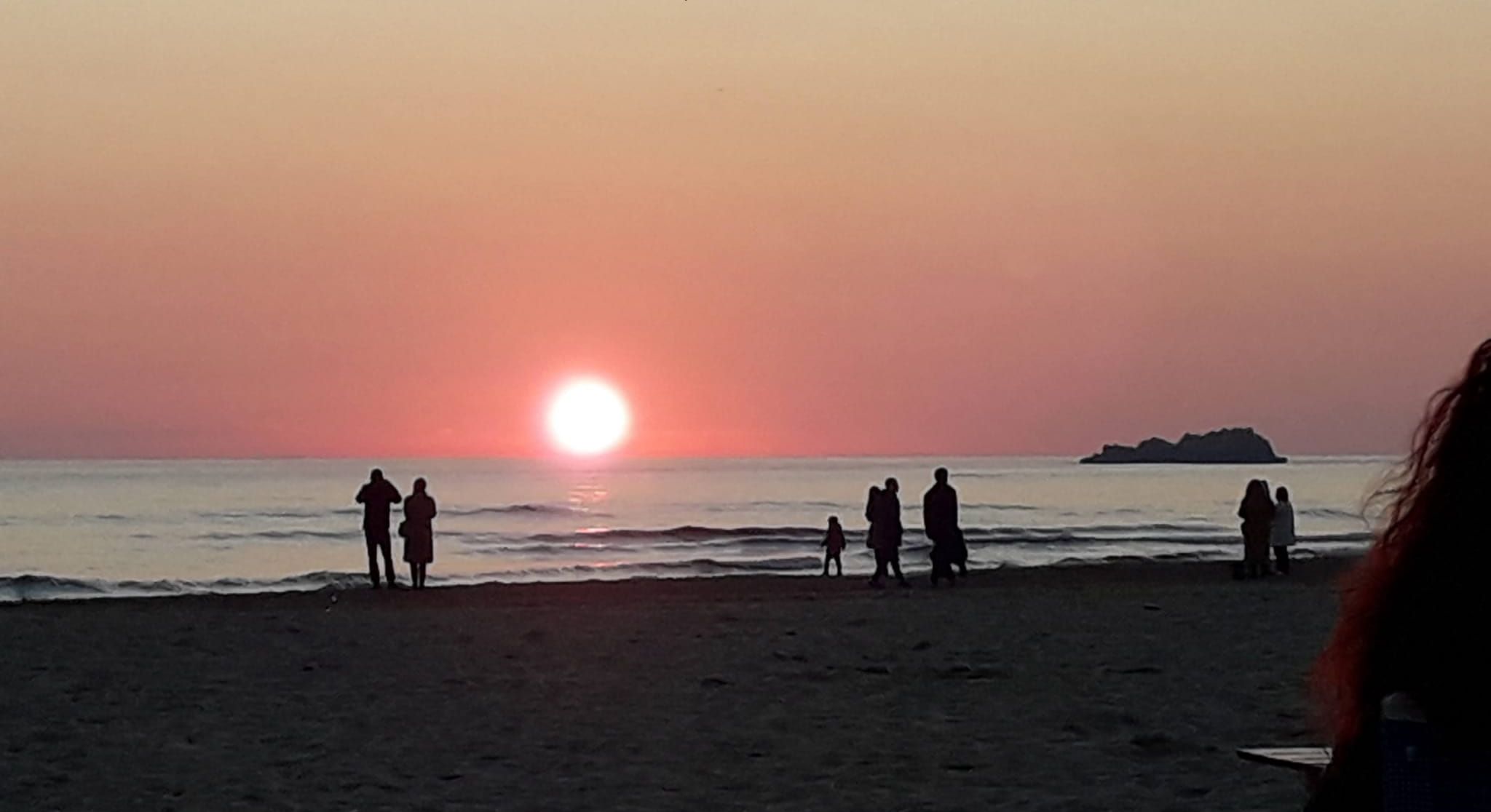 Un coucher de soleil d’hiver sur la plage de Serapio, avec des personnes debout sur le sable.