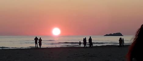 A winter sunset at Serapio Beach with people standing on the sand.