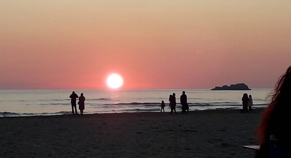 A winter sunset at Serapio Beach with people standing on the sand.