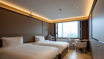 A modern hotel room with two beds, a desk, a chair, and a large window offering a city view.