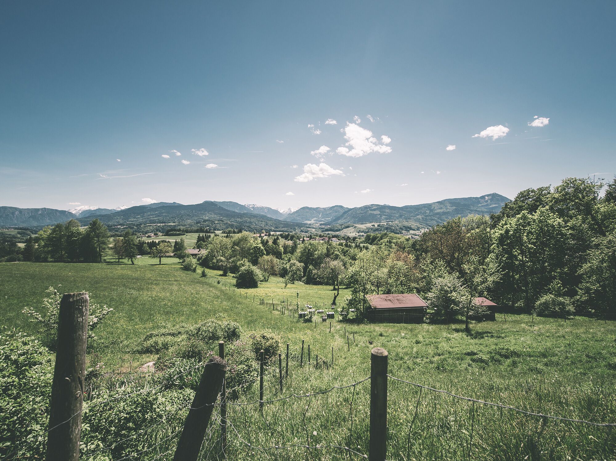 A rural landscape with a fenced field, a small building, and distant mountains under a clear sky.