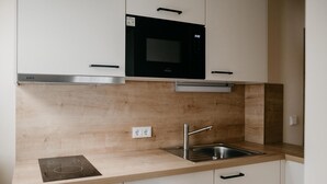 A kitchen with white cabinets, a black microwave, a stainless steel sink, and a wooden countertop. - Gemütliche Ferienwohnung Hochfelln, 40qm, Balkon (Traunstein)