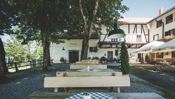 An outdoor seating area with wooden benches and tables, surrounded by trees and buildings with traditional architecture. - Gemütliche Ferienwohnung Hochfelln, 40qm, Balkon (Traunstein)