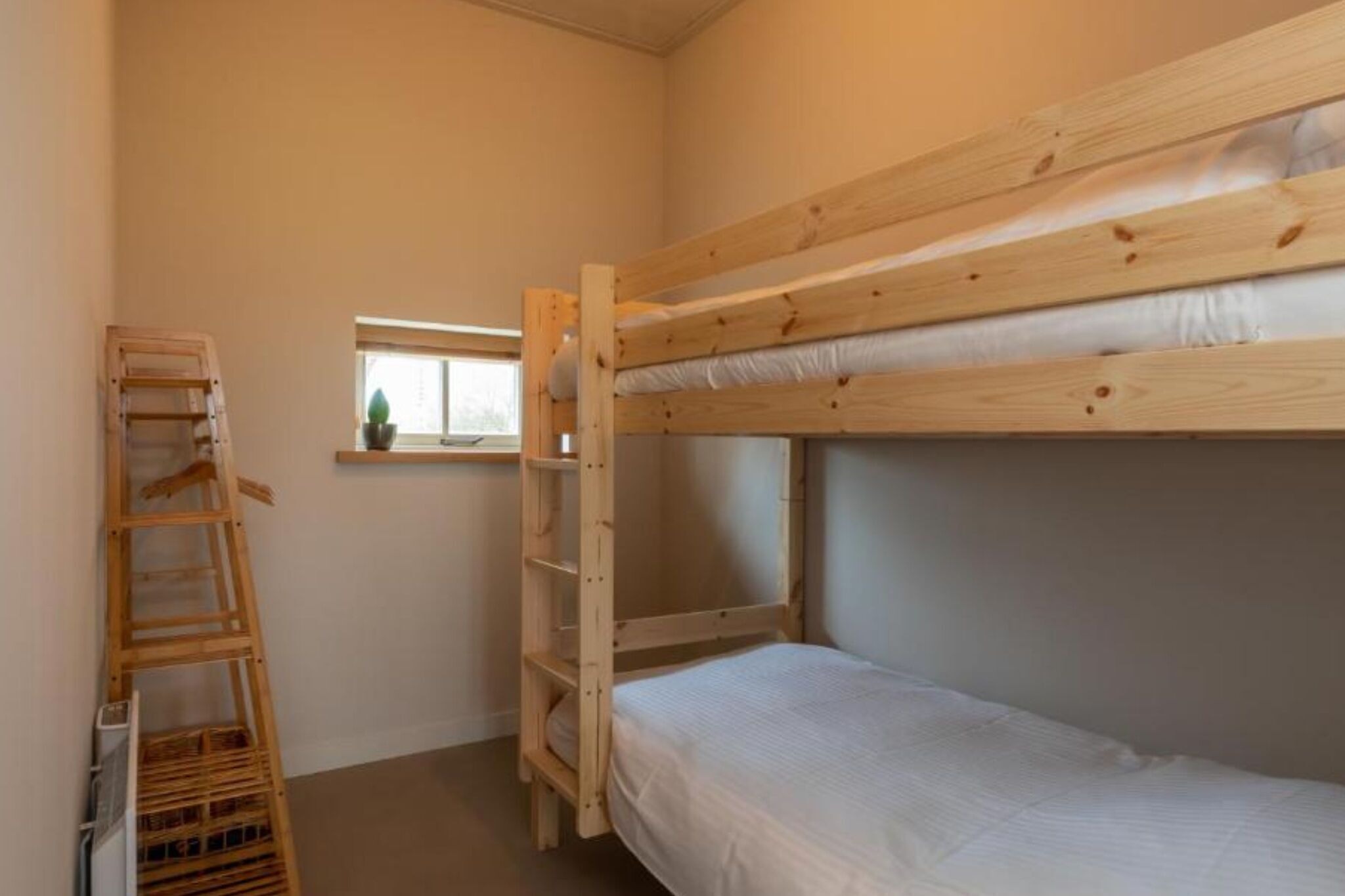 A bunk bed room with a wooden ladder and a window.