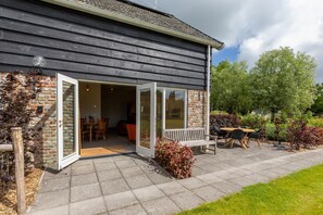 Una casa con un patio amueblado con mesa y sillas, un banco y una puerta que da a un espacio interior.