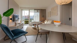 Un salon moderne avec une table à manger ronde, un canapé, un téléviseur et une grande fenêtre avec des rideaux.