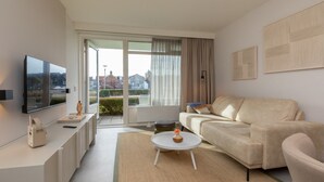 Un salon moderne avec un canapé, une table basse, un téléviseur à écran plat et une grande fenêtre avec des rideaux.