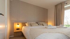 Un lit bien fait, avec une tête de lit, une lampe de chevet et des serviettes pliées posées sur le lit.