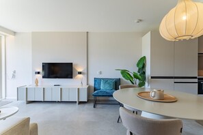 A modern living room with a flat-screen TV, a dining table with chairs, a sofa, and a large plant.