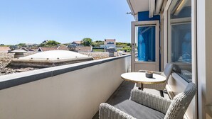 A balcony with a table and chairs, a view of the sea, and a building in the background.