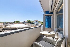 A balcony with a table and chairs, a view of the sea, and a building in the background.