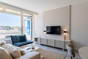A modern living room with a large TV, a sofa, a coffee table, and a dining area.