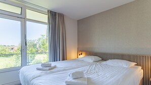 Habitación de hotel con una cama grande, dos almohadas, una mesita de noche con lámpara y una ventana con cortinas.