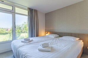 A hotel room with a large bed, two pillows, a nightstand with a lamp, and a window with curtains. - Zoutelande Retreat by Sea (Zoutelande)