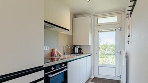 A compact kitchen with a built-in oven, a coffee maker, and a window that opens to a balcony.