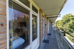 A narrow balcony with a glass door leading to a room, a brick wall, and a metal railing.