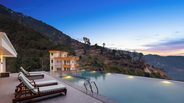 Une piscine avec des chaises longues et un bâtiment doté d’un balcon donnant sur un paysage montagneux.