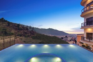 Relax by the infinity pool overlooking the mountainous landscape and cityscape.