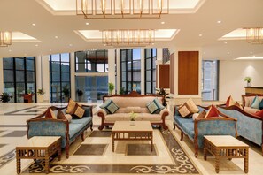 Relax in our elegant lobby, featuring a cozy seating area with a sofa and armchairs, surrounded by large windows and a decorative chandelier.