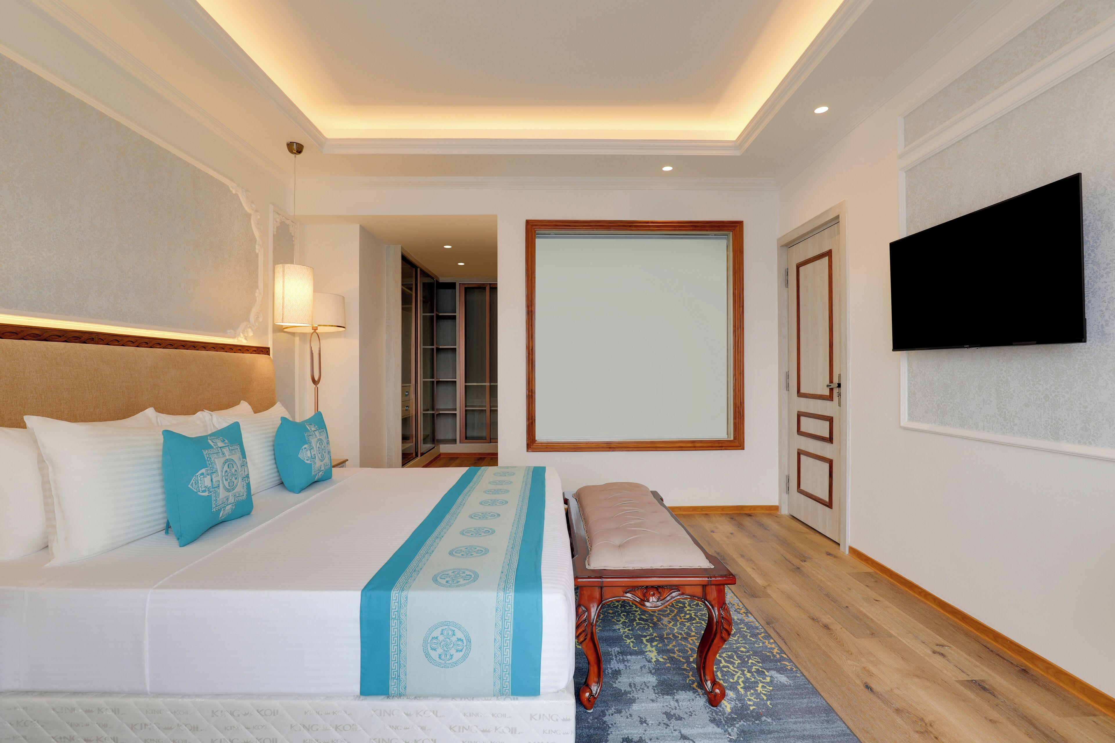 A hotel room with a large bed, bedside table, lamp, and a television on the wall.