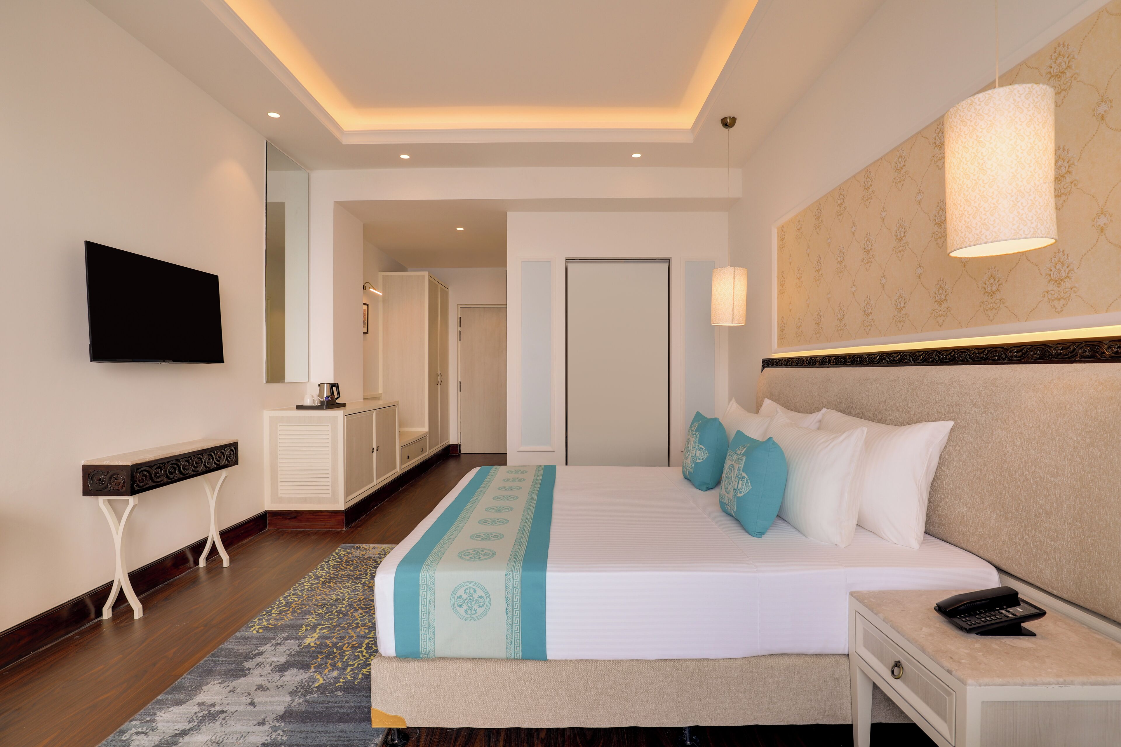 A hotel room with a large bed, bedside table, and a flat-screen TV mounted on the wall.