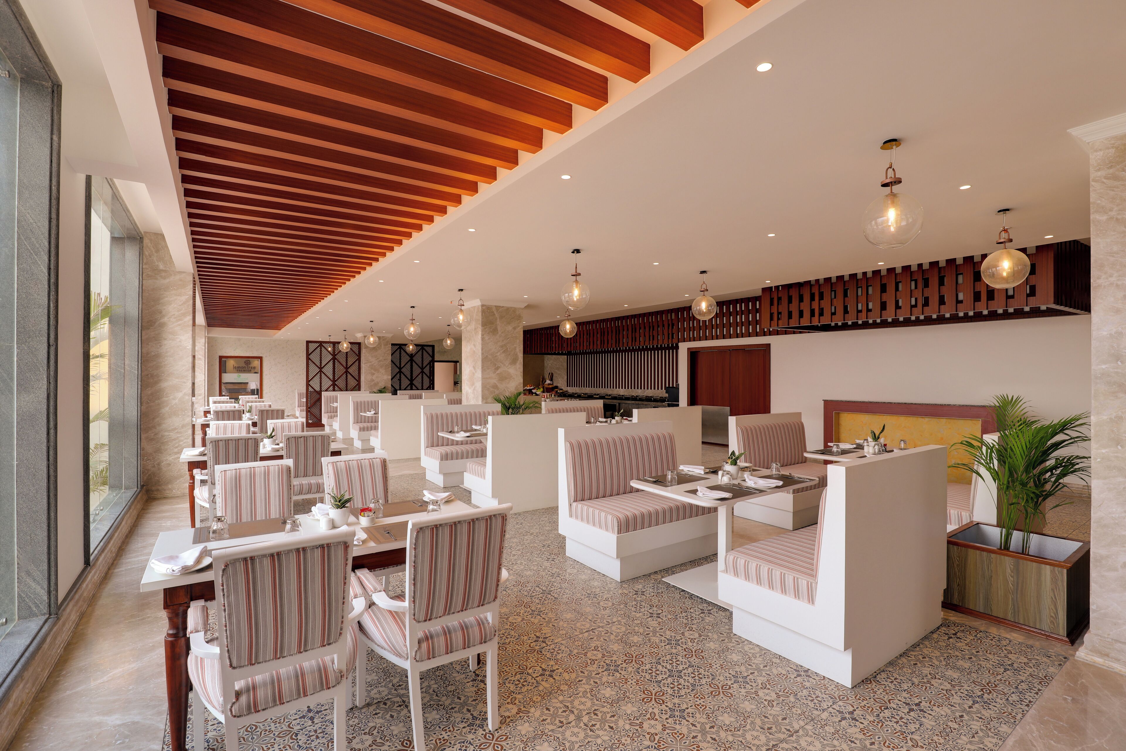 A modern hotel lobby with striped seating, a high ceiling with wooden slats, and a large TV screen.
