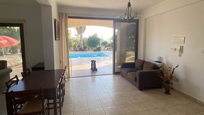 A spacious living area with a dining table and chairs, a sofa, and a view of a swimming pool through a glass door. - Villa Ariadni - Luxurious Villa with Spectacular Views and Private Pool! (Pissouri)