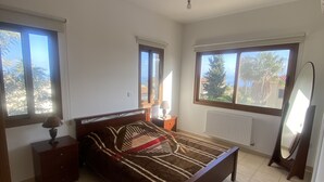 A bedroom with a bed, a nightstand, a lamp, a radiator, and a window with a view of trees. - Villa Ariadni - Luxurious Villa with Spectacular Views and Private Pool! (Pissouri)
