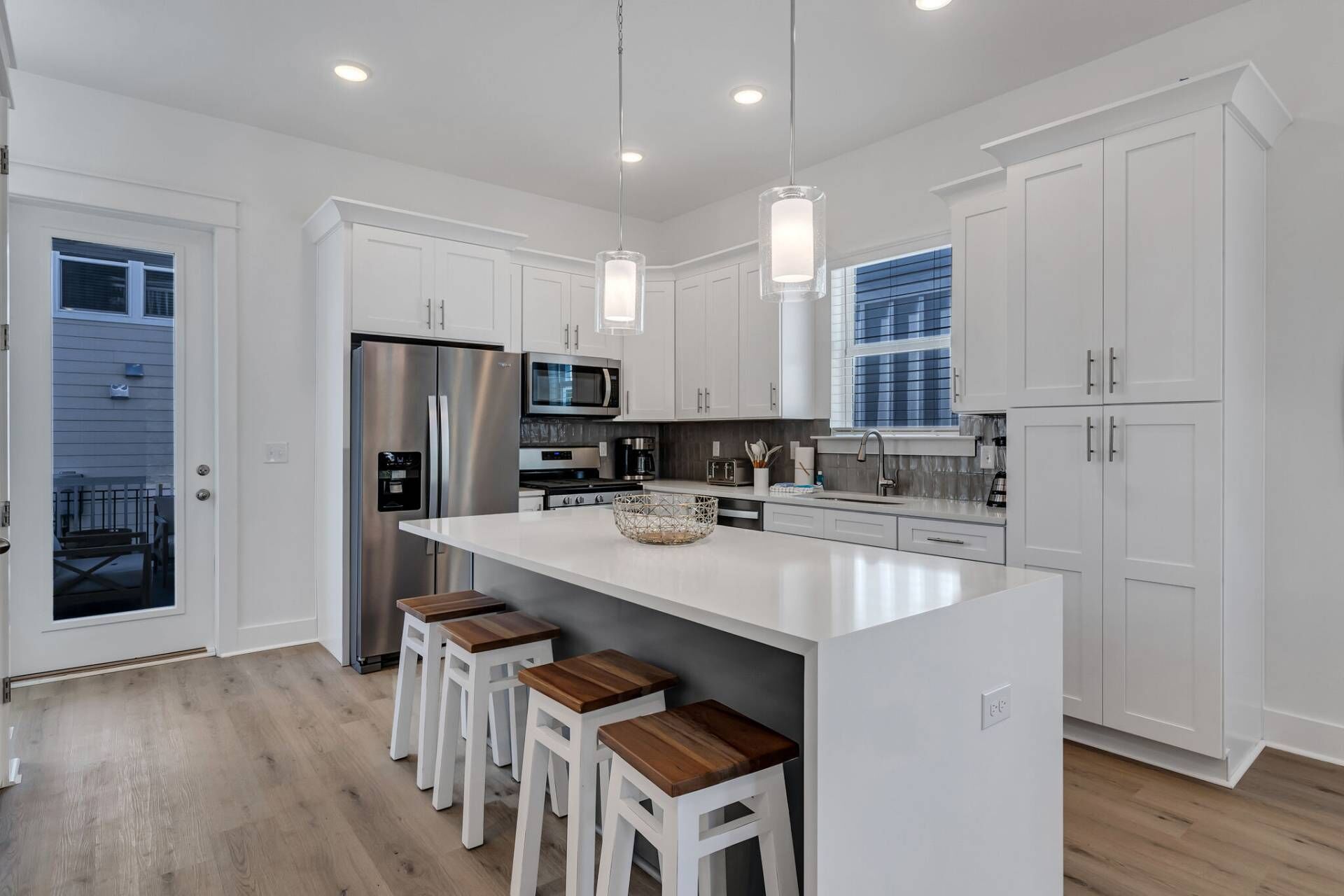 A modern kitchen with white cabinetry, stainless steel appliances, and a central island with stools.