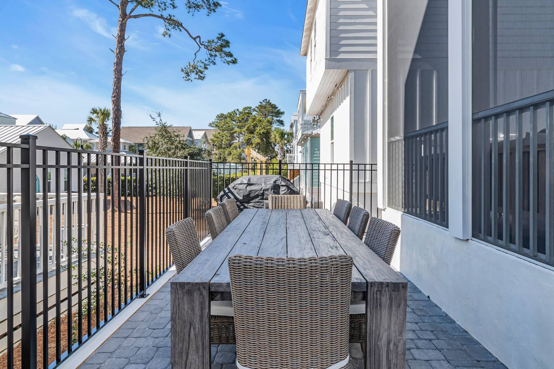 An outdoor patio with a wooden table and wicker chairs, surrounded by a black metal fence.