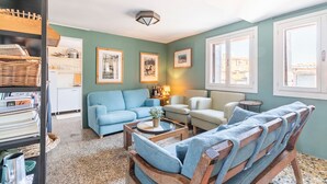 A cozy living room with a blue sofa, a wooden bench, and a coffee table. There are framed pictures on the wall and a window with a view of buildings. - Cà Formosa (Venice)