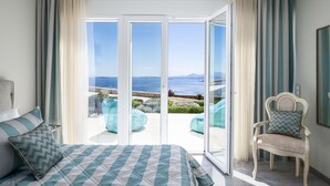 Quarto com cama, uma cadeira e vista para o mar através de grandes portas de vidro.